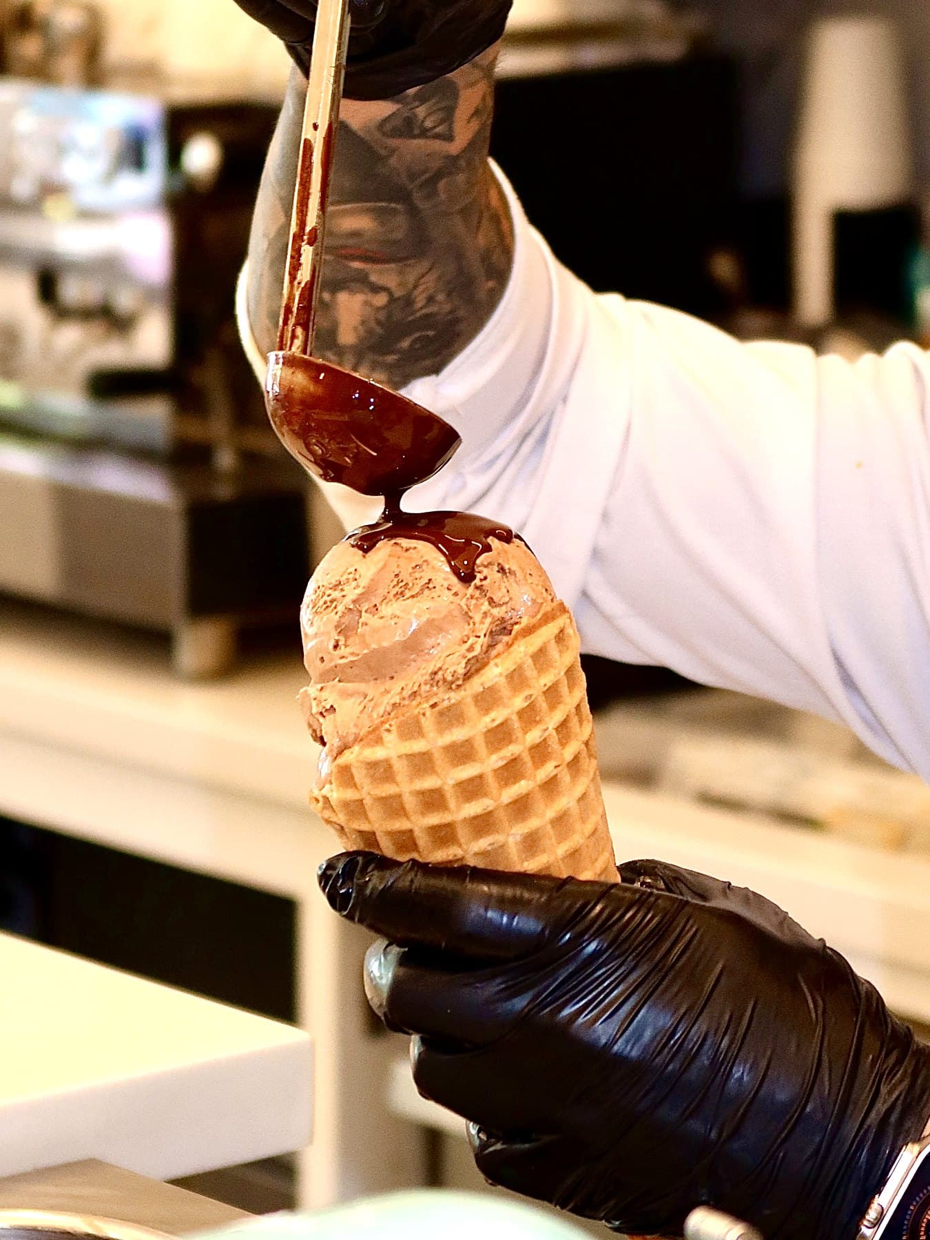 Chocolate being poured over ice cream in a waffle cone