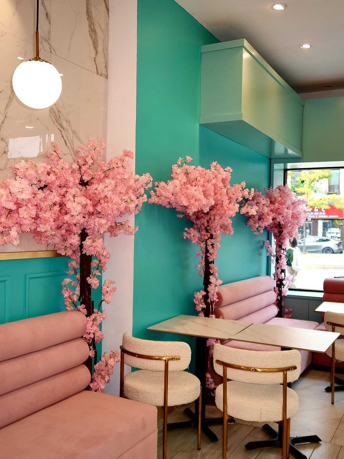 Cherry blossom trees over pink velvet banquettes and marble tables against a teal wall