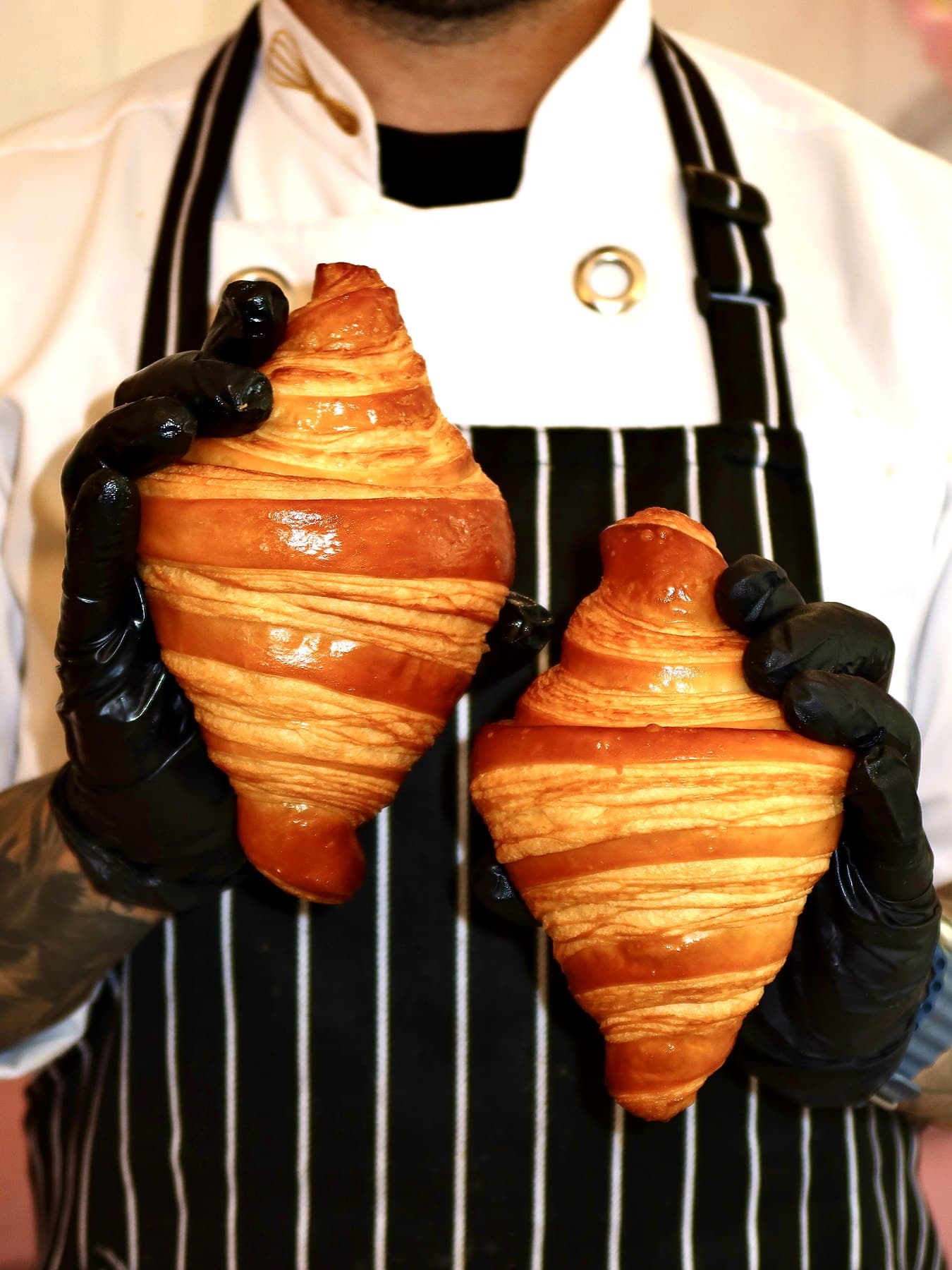 Can holding two fresh croissants against his striped apron