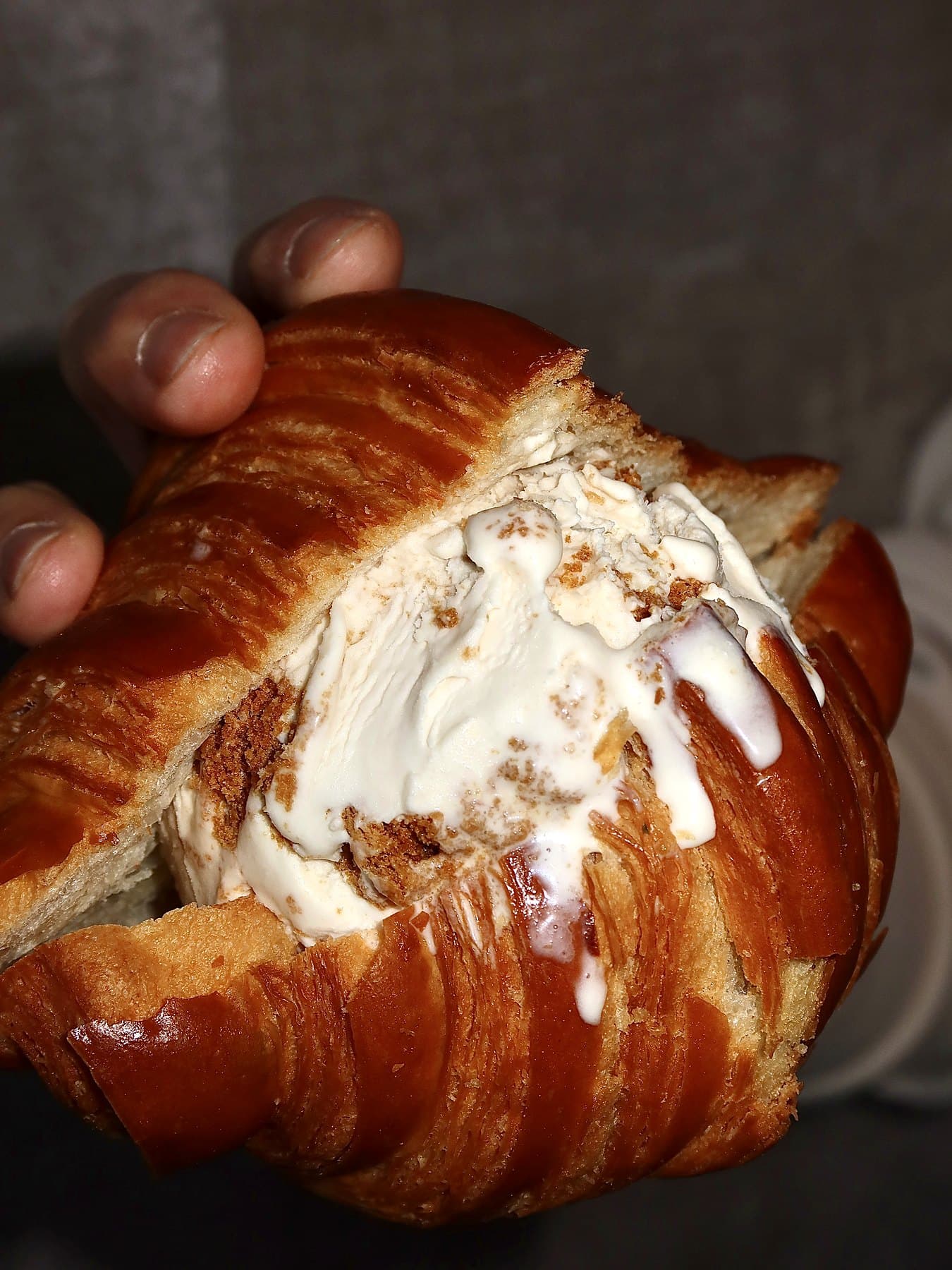 A croissant ice cream sandwich held in one hand
